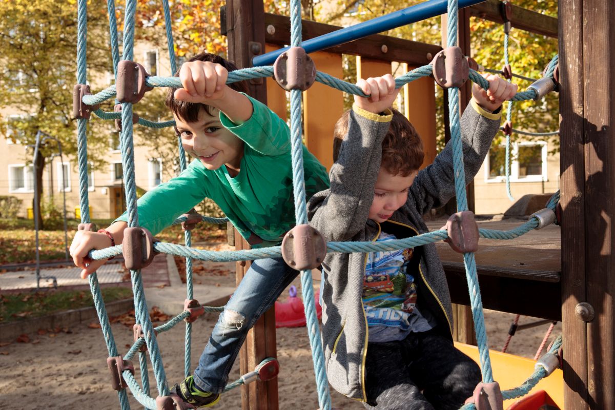 Zwei Jungen klettern konzentriert an einem Kletternetz auf dem Spielplatz.
