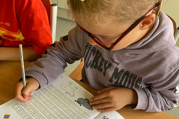 Mädchen mit Brille schreibt konzentriert auf einem Übungsblatt.