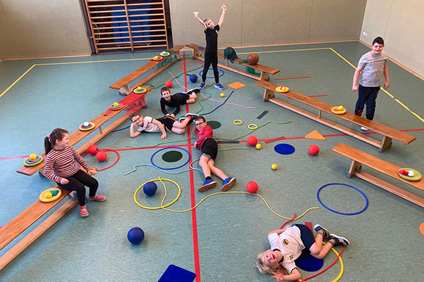 Kinder spielen fröhlich in einer Turnhalle mit Sportgeräten.