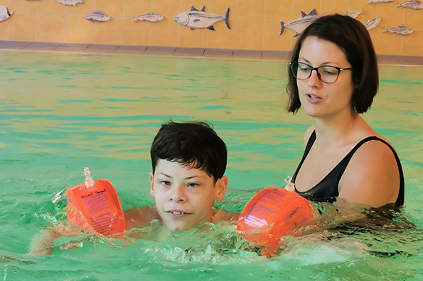 Junge schwimmt mit Schwimmflügeln, begleitet von einer Frau.
