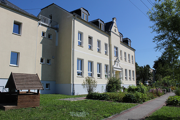Außenansicht eines gelben Schulgebäudes mit Spielhaus im Garten.